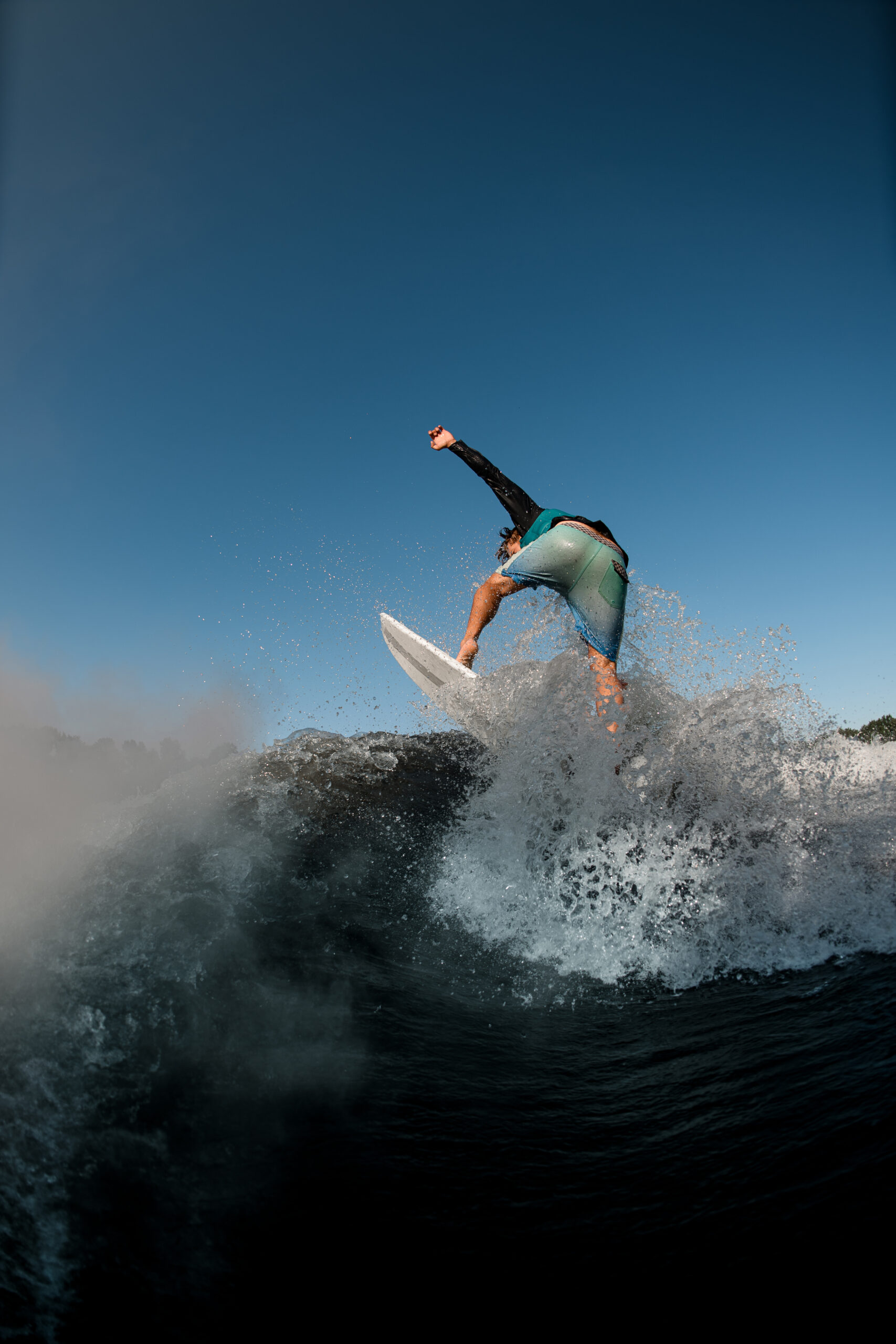 Wet man wakesurfer balances on splashing river wave against the blue sky